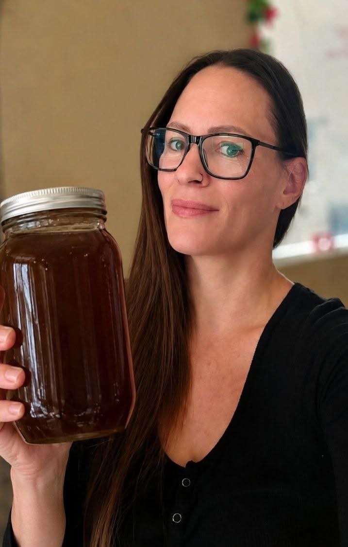 Christina holding a jar of raw local wildflower honey with a window in the background.